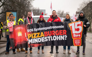 Mark Baumeister, Yasmin Fahimi, Guido Zeitler und andere halten ein großes Transparent in der Hand. Sie stehen auf der Straße vor einem Lautwagen. 