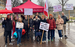 Eine Gruppe Streikender mit Schildern stehen in der Stuttgarter Innenstadt vor einem roten Pavillon mit NGG-Logo. 