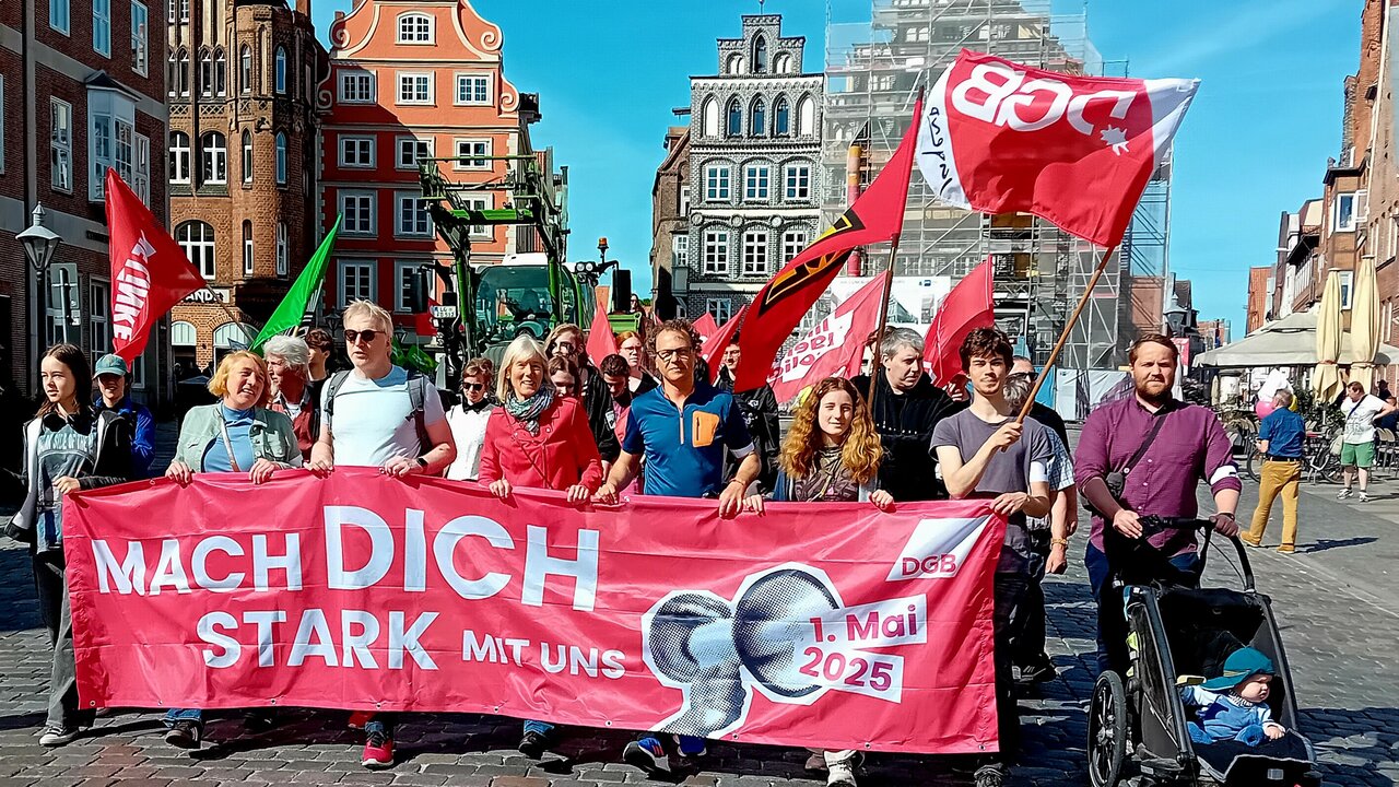 1_Mai_2025_Kiel Menschen tragen das Frontbanner des 1. Mai-Umzugs in Kiel.