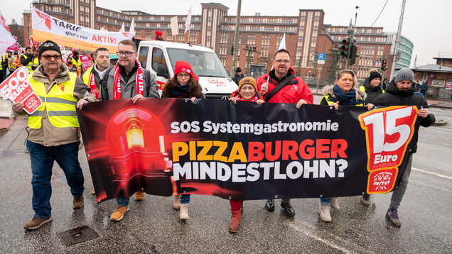Mark Baumeister, Yasmin Fahimi, Guido Zeitler und andere halten ein großes Transparent in der Hand. Sie stehen auf der Straße vor einem Lautwagen. 