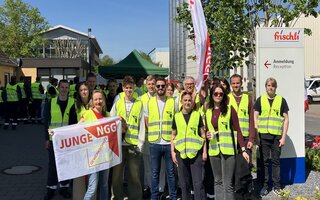 Eine Gruppe Menschen mit neongelben Streikwesten. Sie halten die Fahne von jungeNGG.