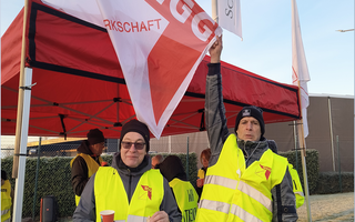 Zwei Beschäftigte in neongelben Streikwesten halten eine NGG-Fahne.