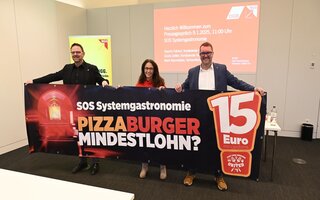 Guido Zeitler, Yasmin Fahimi und Mark Baumeister halten ein Transparent auf dem "Pizza, Burger, Mindestlohn?" steht.