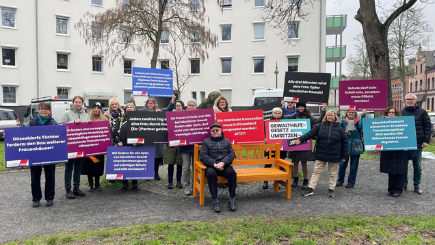 Eine Gruppe von Menschen hält Schilder gegen Gewalt an Frauen nach oben.
