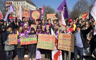 Eine Gruppe von Frauen und Männern posiert am 8. März für ein Gruppenfoto. Sie halten Schilder mit feministischen Sprüchen. 