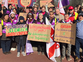Eine Gruppe von Frauen und Männern posiert am 8. März für ein Gruppenfoto. Sie halten Schilder mit feministischen Sprüchen.
