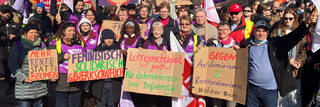 Eine Gruppe von Frauen und Männern posiert am 8. März für ein Gruppenfoto. Sie halten Schilder mit feministischen Sprüchen.