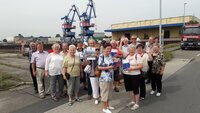 Eine Seniorengruppe steht vor Hafenkränen.