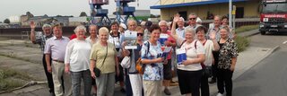Eine Seniorengruppe steht vor Hafenkränen.