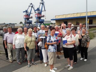 Eine Seniorengruppe steht vor Hafenkränen.