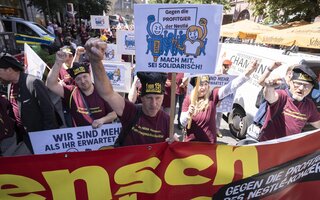 Menschen tragen ein Banner auf dem "Mensch vor Marge" steht. 