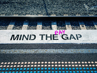 Auf dem Bild sieht man eine Bahnsteigkante auf der in weiß "Mind the Gap" steht. zwischen the und gap ist in pink das Wort "pay" eingefügt. 