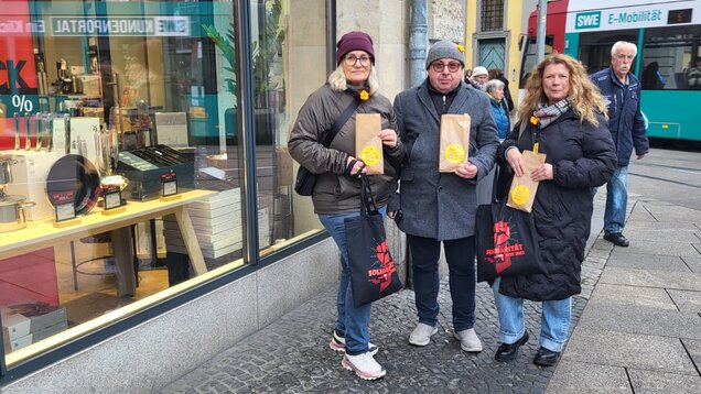 Drei Menschen auf der Straße halten Lunchtüten mit der Aufschrift "Belästigung kommt uns nicht in die Tüte"