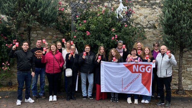 Eine Gruppe Menschen hält  eine Rote Karte mit der Aufschrift "Nein zu Gewalt an Frauen" hoch