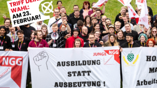 Eine Gruppe Jugendlicher mit Transparenten steht auf einer Wiese.