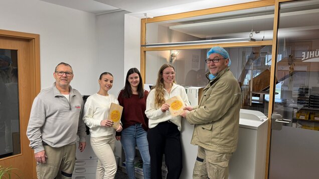 Eine Gruppe Menschen steht in einem Raum. Zwei Frauen halten Lunchtüten mit der Aufschrift "Belästigung kommt uns nicht in die Tüte"