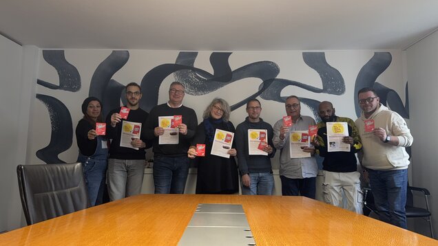 Eine Gruppe Menschen hält einen Flyer und eine Rote Karte mit der Aufschrift "Nein zu Gewalt an Frauen" hoch